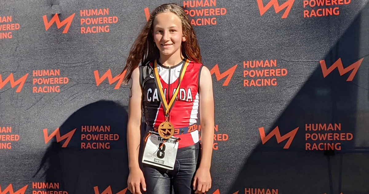 A young athlete stands in front of the podium with her medal.